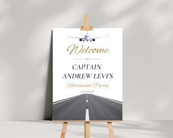 Puede incluir: Un letrero rectangular blanco sobre un caballete de madera con un gráfico de un avión y una pista de aterrizaje. El texto dice: Welcome TO CAPTAIN ANDREW LEVI'S Retirement Party 11/14/2026. Welcome y Retirement Party están en letra dorada.