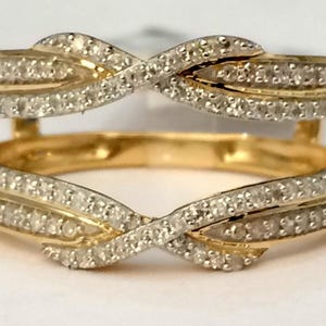 May include: A yellow gold ring guard featuring two bands connected by a bridge. Each band displays a crossover infinity design encrusted with small, clear, round-cut stones. The metal has a polished finish, and the stones cover the front surface.