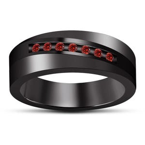 Op de afbeelding: Een matzwarte bandring met een horizontale kanaalinleg bezet met zeven kleine, ronde, felrode edelstenen. De ring heeft een gladde, solide constructie met een gepolijste binnenzijde en een breed, plat profiel aan de bovenzijde.
