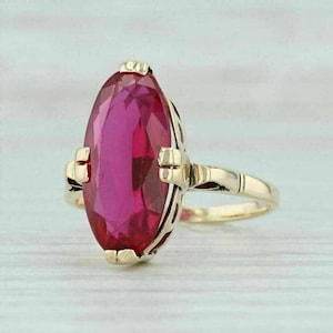 Op de afbeelding: Een gouden ring met een grote, markiesgeslepen, levendig roze edelsteen in een zetting met vier pootjes. De band is gemaakt van gepolijst geelgoud en heeft een slank ontwerp dat taps toeloopt naar de achterkant van de ringzetting.