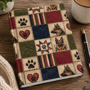 May include: A hardback journal featuring a quilted-style patchwork cover with alternating squares of red, navy blue, and olive green. The design includes illustrations of German Shepherd dogs, black paw prints, red hearts, and multi-coloured stripes.