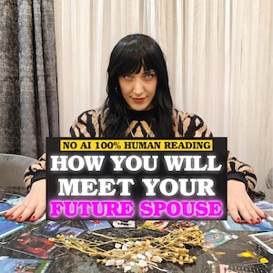 May include: A person with dark hair wearing a black and tan patterned sweater sits behind a table covered in tarot cards and dried flowers. A black sign with white and pink text reads: NO AI 100% HUMAN READING HOW YOU WILL MEET YOUR FUTURE SPOUSE.