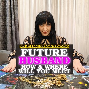 May include: A person with dark hair wearing a black and tan patterned sweater, positioned behind a table covered in tarot cards and dried flowers. A black sign with white and pink text reads: NO AI 100% HUMAN READING FUTURE HUSBAND HOW & WHERE WILL YOU MEET.