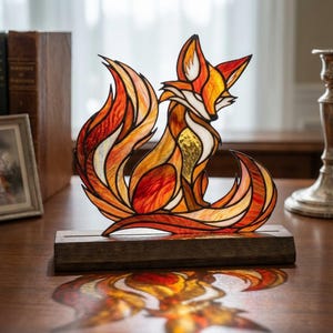 Peut inclure: Une sculpture de renard en vitrail composée de segments de verre orange, rouge et jaune vifs avec des accents blancs, fixée sur un socle en bois sombre. Le renard est représenté assis avec une grande queue courbée, soulignée par des lignes de plomb.