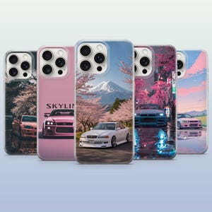 May include: Five smartphone cases featuring automotive designs. The cases display various scenes including a white car with Mount Fuji and cherry blossoms, a pink car with the text SKYLINE, a blue car on a wet street, and a pink car at sunset.