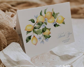 May include: A folded card with a watercolor illustration of lemons on a branch with green leaves and blue flowers. The words "Thank You" are written in script, with the names "Sarah & Chris" and the date "07.26.2025" below. The Ann Green Card Company logo is at the bottom.