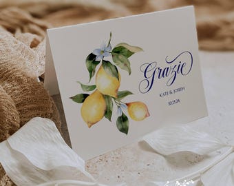 May include: A folded white card with a watercolor illustration of lemons and leaves. The word "Grazie" is written in navy blue script, with "Kate & Joseph" and the date 10.15.24 below. The Ann Green Card Company logo is at the bottom.