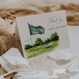May include: A white folded card with a watercolor illustration of a golf course, a green flag, and the text "Thank You FORE EVERYTHING!". The card also features the Ann Green Card Company logo.