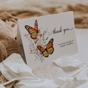 May include: A white folded card featuring a watercolor illustration of two orange and black monarch butterflies perched on pink flowers. The text reads Thank you and IN LOVING MEMORY OF MARY SAMPLE in a black script and serif font.