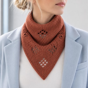 Pode incluir: Um cachecol triangular de malha na cor ferrugem com textura canelada e padrões de renda vazada em forma de diamante. O cachecol é usado em estilo gola, exibindo uma borda frontal pontiaguda e um ponto de tricô consistente em toda a peça.