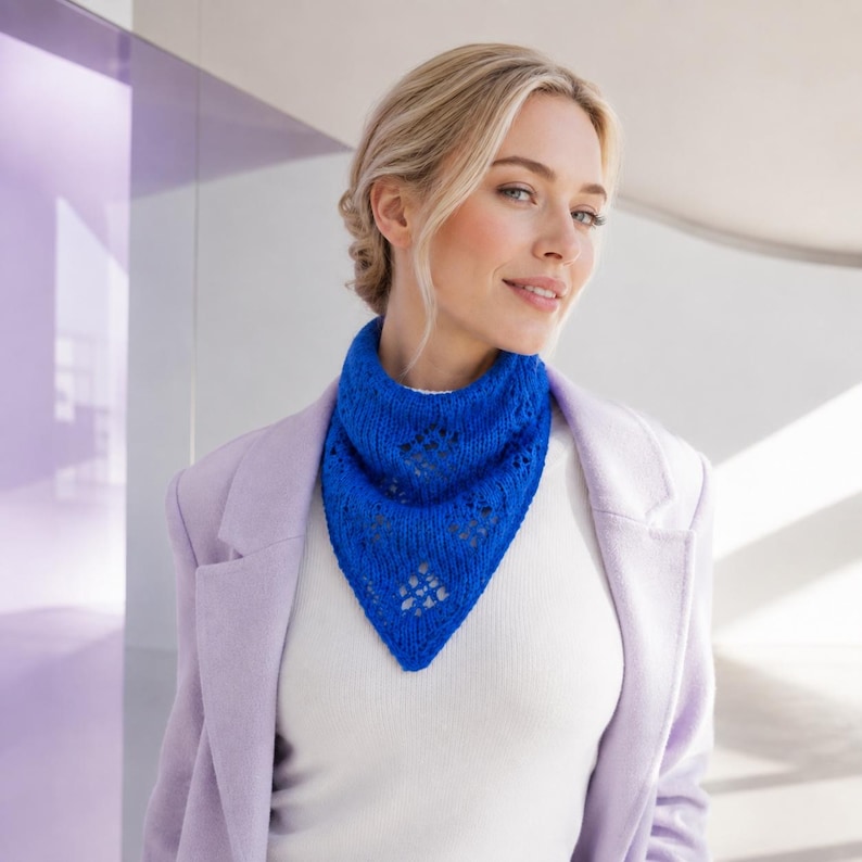 May include: A vibrant royal blue triangular knit scarf featuring a delicate openwork diamond pattern throughout the fabric. The scarf is styled as a neckerchief, resting against a white top and a light lavender blazer, showcasing its texture.