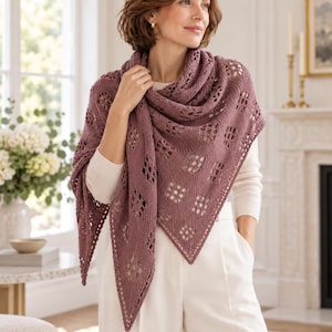 Può includere: Uno scialle triangolare color rosa antico caratterizzato da un intricato motivo in pizzo traforato con rombi ripetuti e un bordo in maglia testurizzata. L'accessorio è drappeggiato sulle spalle, mettendo in risalto la lavorazione.