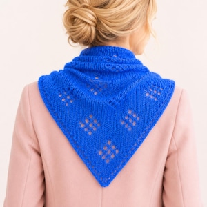 May include: A vibrant royal blue triangular knit shawl featuring a delicate openwork diamond pattern throughout the fabric. The scarf is draped over the shoulders, showcasing a textured stitch design with a pointed bottom edge and ribbed border.