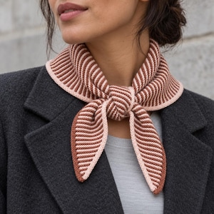 May include: A knitted neckerchief featuring a striped pattern in alternating shades of terracotta brown and pale pink. The accessory has a ribbed texture and is tied in a simple knot at the front, with a solid pale pink border along the edges.