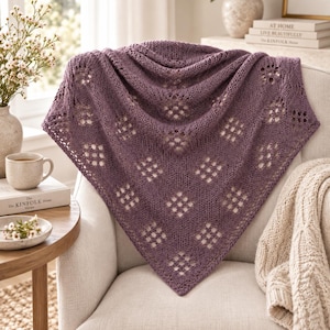 Könnte beinhalten: Ein dreieckiges Stricktuch in einem staubigen Violettton mit einem sich wiederholenden rautenförmigen Lochmuster. Das Textil hat eine weiche, strukturierte Optik mit einer spitz zulaufenden Unterkante und einem breiten oberen Rand.