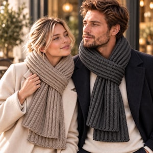 May include: A beige ribbed knit scarf worn over a cream coat and a dark charcoal gray ribbed knit scarf worn over a white sweater and a dark navy blue coat. Both scarves feature a thick, vertical ribbed texture and are wrapped around the neck.