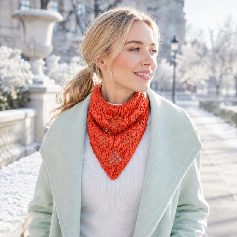 May include: A bright orange triangular knit scarf featuring a delicate openwork diamond pattern throughout the fabric. The scarf is worn around the neck over a white top and a light mint green coat, showcasing a textured stitch design.