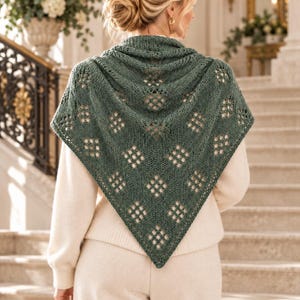 Peut inclure: Un châle en tricot triangulaire de couleur vert sauge profond présentant un motif complexe de losanges ajourés sur tout le tissu. Le châle est drapé sur les épaules, mettant en valeur un design en maille texturée avec un bord inférieur pointu.