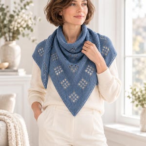 May include: A blue triangular knit shawl featuring a repeating diamond-shaped eyelet pattern and a ribbed border. The shawl is draped around the neck and shoulders, showcasing a textured yarn construction with a pointed hem at the centre front.