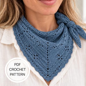 Puede incluir: Un pañuelo triangular de ganchillo en color azul polvoriento con un intrincado patrón de encaje calado y un borde festoneado. El pañuelo está anudado a un lado. Una insignia blanca circular en la esquina contiene el texto PDF CROCHET PATTERN.