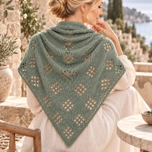 May include: A sage green triangular knit shawl featuring a repeating diamond-shaped lace pattern with openwork details. The shawl is draped over the shoulders, showcasing a textured stitch design that tapers to a point at the centre back.
