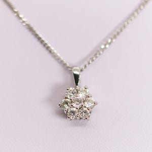 Könnte beinhalten: Eine silberfarbene Halskette mit einem Anhänger aus sieben runden, klaren, facettierten Steinen, die in einem Blumenmuster angeordnet sind. Der Anhänger hängt an einer zarten, dünnen silberfarbenen Kette, die oben an der Fassung befestigt ist.