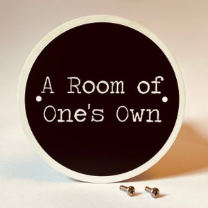 May include: A round black sign with white lettering that reads "A Room of One's Own".