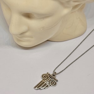 May include: A silver necklace with a pendant shaped like a stylised column with a scroll design. The necklace is on a mannequin's neck.