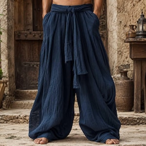 May include: Deep navy blue loose-fitting trousers featuring a gathered waist with a long, integrated fabric tie belt. The pants have a textured, crinkled appearance, wide legs that drape fully to the floor, and visible side pockets.