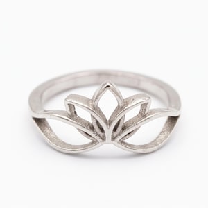 May include: A silver-toned metal ring featuring a cutout design shaped like a lotus flower. The band is smooth and circular, transitioning into a symmetrical, openwork floral motif at the top, showcasing clean lines and a polished metallic finish.