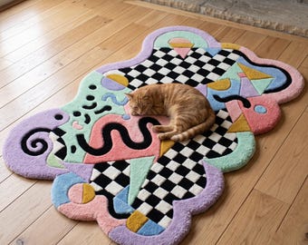 May include: An irregularly shaped area rug featuring a black and white checkerboard pattern combined with abstract shapes in pastel pink, lavender, mint green, and yellow. An orange tabby cat is lying in the center of the textured, tufted rug.