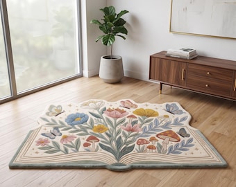 May include: A shaped area rug designed to look like an open book. The surface features a colorful illustration of various flowers, mushrooms, and butterflies in shades of blue, pink, yellow, and red, set against a cream-colored background.