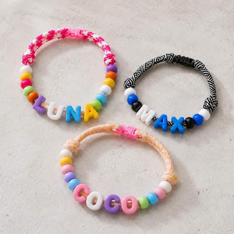 May include: Three bracelets featuring colorful cords and plastic letter beads. One bracelet has a pink and white cord with the name LUNA, one has a black and white patterned cord with the name MAX, and one has a peach cord with the name COCO.