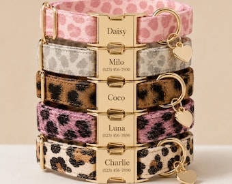 May include: A stack of five pet collars featuring various leopard print patterns in pink, gray, brown, and tan. Each collar has a gold-tone metal buckle engraved with a name and phone number, and a gold-tone heart-shaped charm attached to a D-ring.