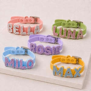 May include: Five adjustable silicone collars in pastel colors, each featuring personalized names spelled out in sparkling rhinestone letters. The collars include the names BELLA in pink, LUNA in green, ROSIE in purple, MILO in blue, and MAX in yellow.