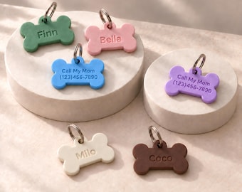 May include: Six bone-shaped pet ID tags in green, pink, blue, purple, cream, and brown. Each tag features a metal ring and engraved text including names like Finn, Bella, Milo, and Coco, or the phrase Call My Mom with a phone number.