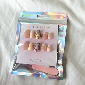 May include: A set of press-on nails in a holographic pouch, featuring a monkey design, yellow stripes, and small yellow flowers on a pink and nude base. The packaging includes the text Size: XS S M L F and Nail Art, along with a small pink nail file.