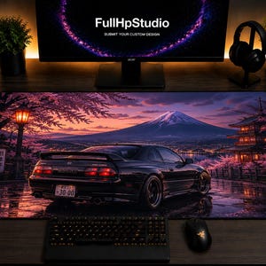 May include: A rectangular desk mat featuring a printed scene of a black sports car parked on a wet road at sunset. The background displays a mountain, a traditional pagoda, and cherry blossom trees. The license plate reads 30-00.