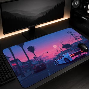 May include: A rectangular desk mat featuring a vibrant digital illustration of a white sports car driving down a palm-lined street at sunset. The scene includes a pink and purple sky, silhouetted buildings, and utility poles in a retro aesthetic.