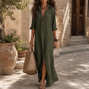 May include: A long-sleeved olive green maxi dress with a button-down collar, a front slit, and a textured finish. The dress is paired with a large, woven tan straw tote bag and a layered beaded necklace featuring a central pendant.