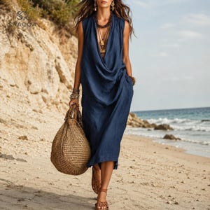 May include: A sleeveless navy blue midi dress with a draped cowl neckline and a loose, flowing silhouette. The garment is paired with a large, round, woven straw handbag, layered beaded necklaces, and brown strappy sandals.