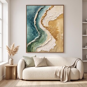 Puede incluir: Una pieza de arte mural rectangular que presenta una escena oceánica abstracta y texturizada con olas en azul cerceta, verde salvia y blanco rompiendo contra una orilla beige arena acentuada con detalles de pan de oro, con marco de madera.