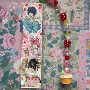 May include: A rectangular bookmark featuring anime character illustrations of L from Death Note and My Melody, paired with a dangling beaded charm strand. The strand includes red and pink strawberry-shaped beads, clear flower beads, and a miniature cupcake charm.