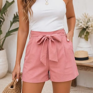 Puede incluir: Shorts de talle alto en color rosa empolvado con un cinturón de tela integrado que se ata con un lazo en la parte delantera central. Los shorts cuentan con una cintura estructurada, bolsillos laterales y una silueta limpia y entallada.