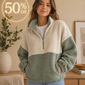 Peut inclure: Un pull en polaire sherpa à blocs de couleurs, composé d'une partie supérieure crème et d'une partie inférieure vert sauge. Le vêtement présente un col montant avec une fermeture éclair argentée, des manches longues et deux poches latérales.