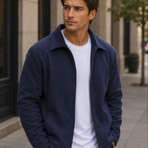 May include: A navy blue zip-up jacket with a classic collar and long sleeves, worn over a plain white crew neck t-shirt. The jacket features a full-length metal zipper down the center and two side pockets, paired with simple black trousers.