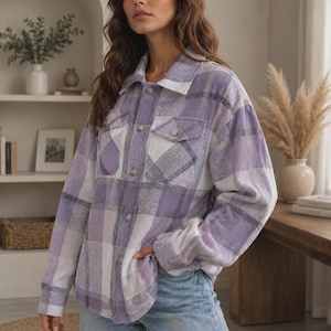 Puede incluir: Una camisa de manga larga con botones y un patrón de cuadros en tonos morado, blanco y gris. La camisa cuenta con un cuello clásico, dos bolsillos en el pecho con solapas abotonadas y un cierre frontal con botones de color claro.