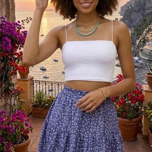 Puede incluir: Un top corto blanco de tirantes finos combinado con una falda azul de volantes con un pequeño estampado floral blanco. La falda tiene una cintura elástica y una silueta acampanada que cae por encima de la rodilla.