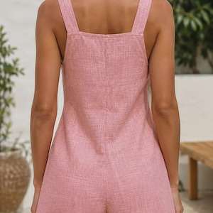 Puede incluir: Un mono corto de color rosa empolvado con escote cuadrado, tirantes anchos y una textura tejida visible. La prenda presenta un diseño de espalda recta y perneras cortas, ofreciendo una silueta sencilla y limpia sin patrones ni adornos añadidos.