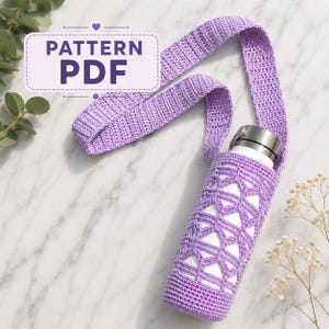 May include: A white water bottle encased in a lavender crocheted sleeve with a matching long shoulder strap. The sleeve features a geometric openwork pattern. A rectangular label with a purple border displays the text PATTERN PDF.